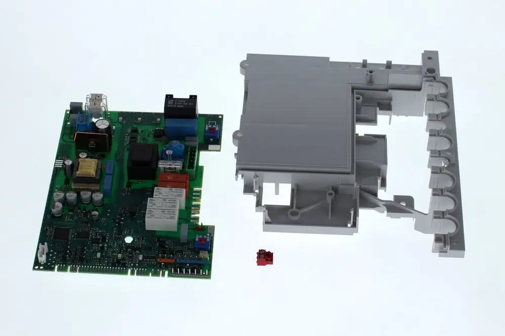 Bosch Leiterplatte in grün mit verschiedenen elektronischen Komponenten, darunter Relais und Kondensatoren, neben einem grauen Gehäuseteil und einem kleinen roten Bauteil.